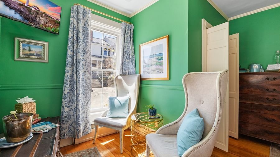 Bright sitting room with green walls, high-back chairs, and large windows at Hartstone Inn.