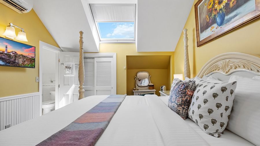 A room with double bed with designed pillows on top, wall art, and cozy yellow decor at Hartstone Inn.