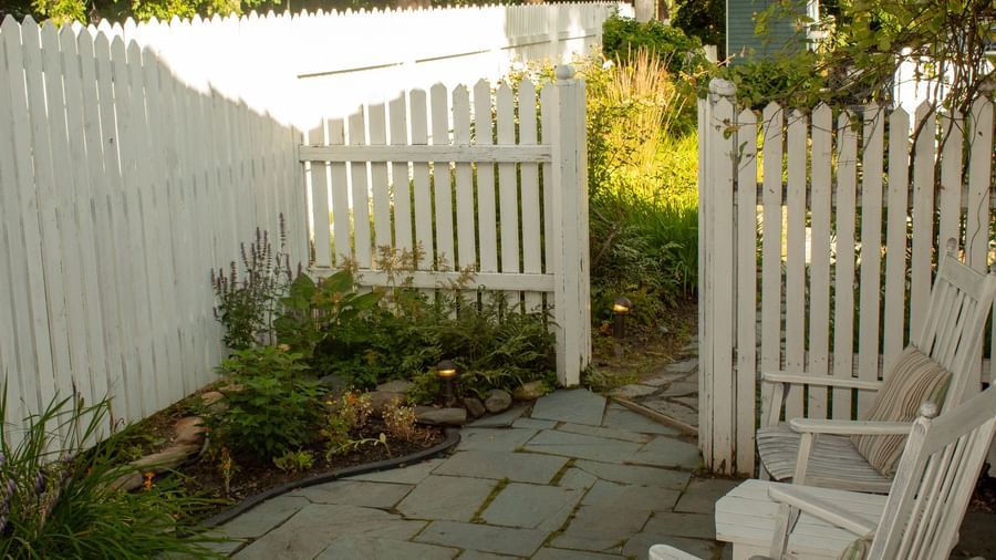 Private garden patio at Hartstone Inn with white picket fence, stone path and wooden bench seating.