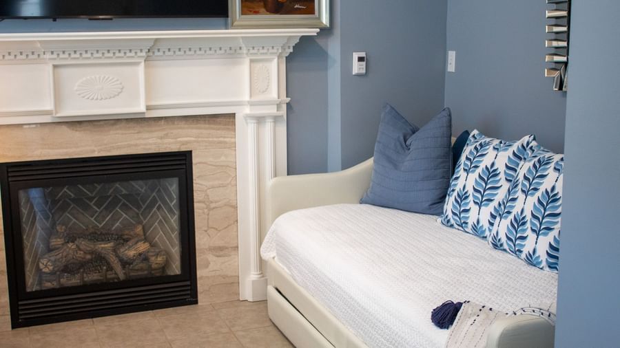 Reading area with white daybed, blue pillows, fireplace with white mantel and TV above at Hartstone Inn.