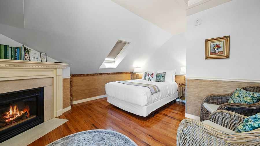 A room with fireplace, cushioned chairs, and slanted ceiling at Hartstone Inn.