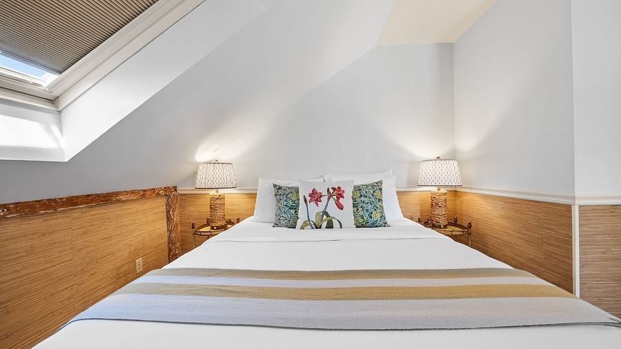 A bedroom with sloped ceiling with floral bed pillows at Hartstone Inn