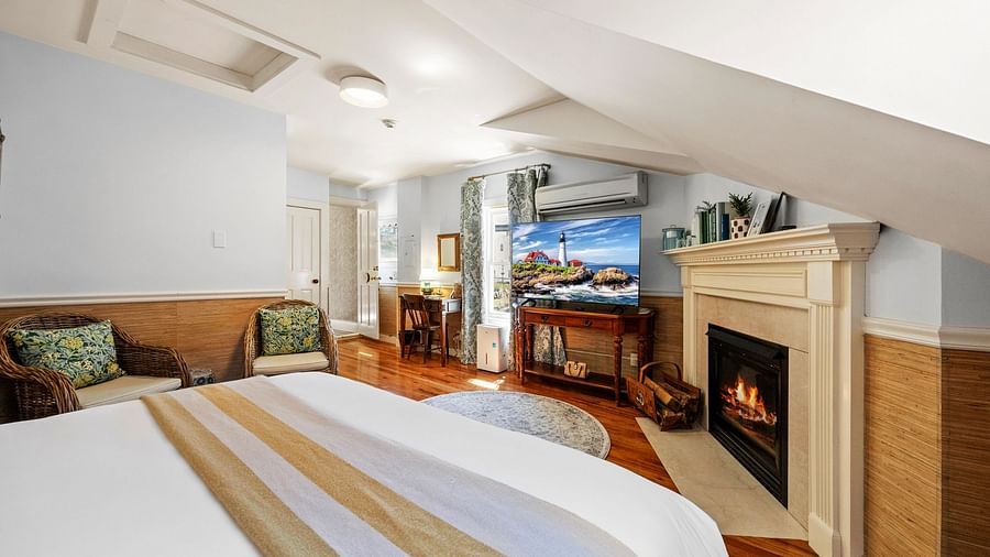 A room with king size bed, fireplace, a pair of chairs placed near the bed and a tv at Hartstone Inn.