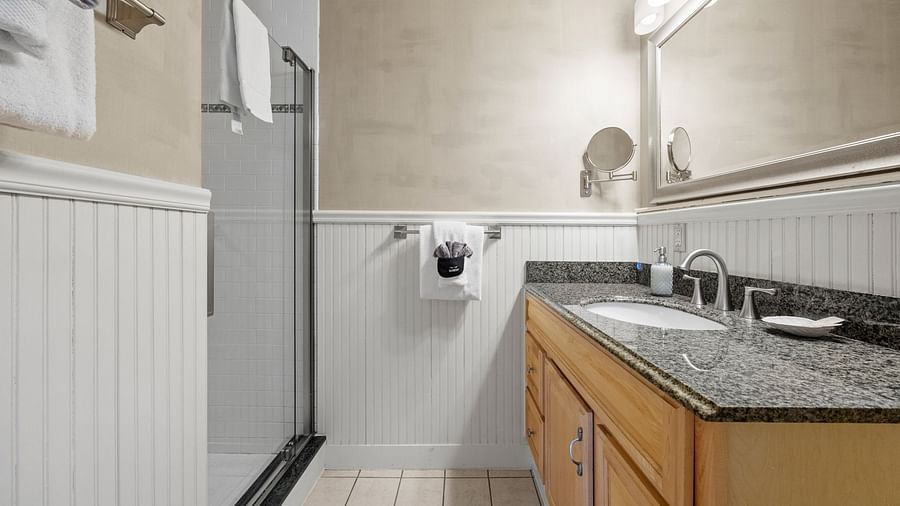 A bathroom with shower area, a small mirror, towels and a sink at Hartstone Inn.