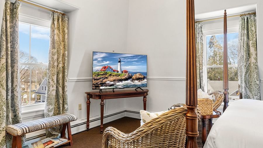 Room featuring bed, wall-mounted TV, chair, books placed near the big glass window at Hartstone Inn