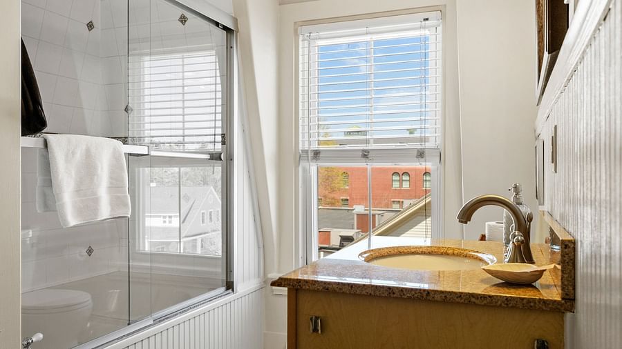 Compact bathroom with window view, white fixtures, and tan vanity at Hartstone Inn