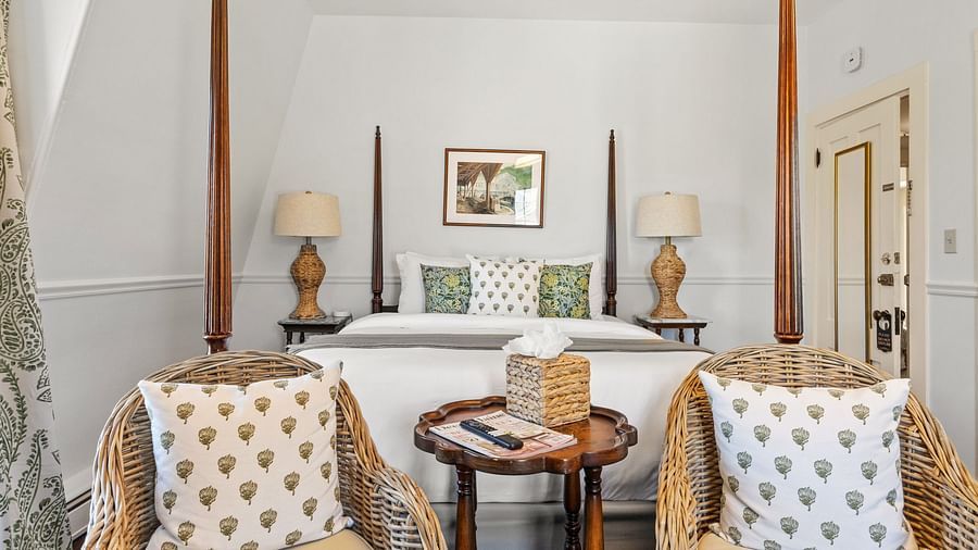 A bedroom with a four-poster bed and cosy sitting area with two armchairs at Hartstone Inn.