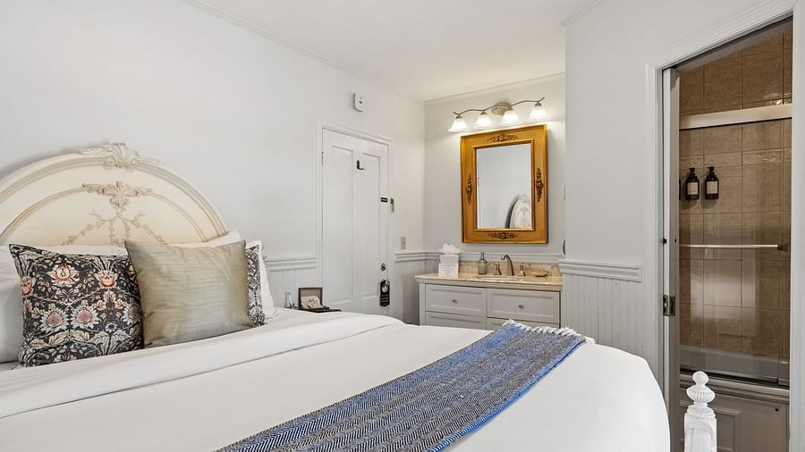 A bedroom with ornate headboard, a mirror, table and blue-accented runner at Hartstone Inn