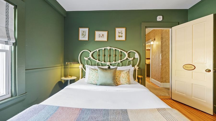 Green-walled bedroom with white iron bed with framed arts in the wall at Hartstone Inn.