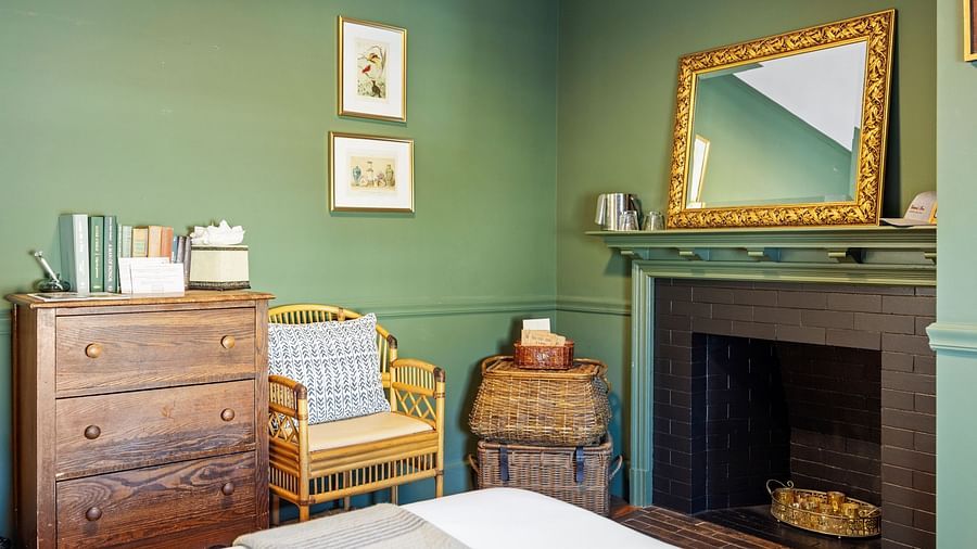 Green-toned bedroom with vintage mirror, fireplace, and wooden table at Hartstone Inn