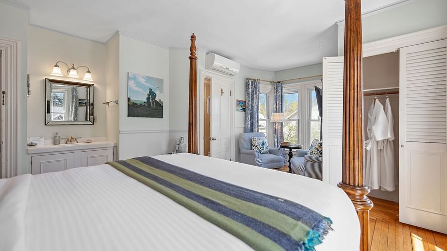 Elegant guest room with canopy bed, a closet hanging a pair of bathrobe and a sitting area in the corner at Hartstone Inn