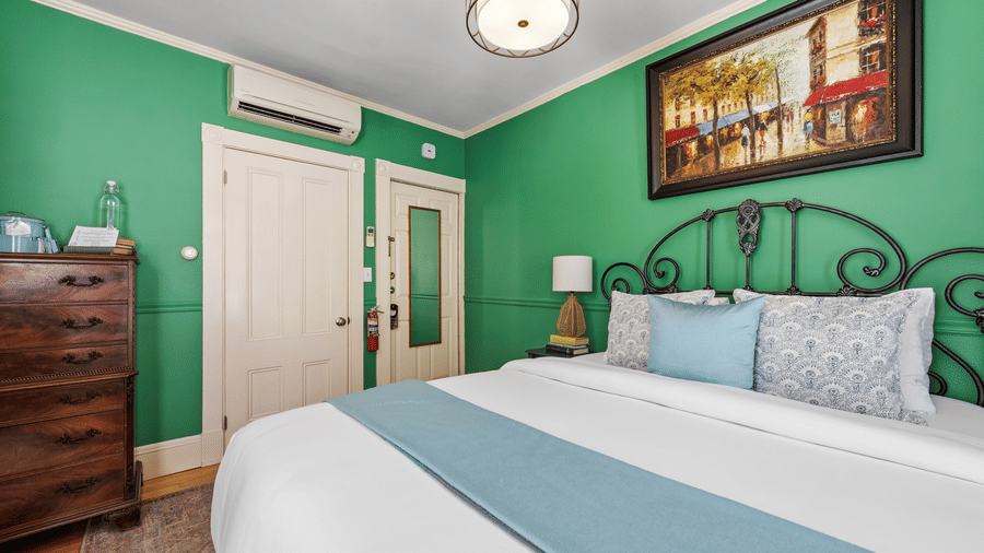 A bedroom with green walls, white bedding, and a decorative iron bed frame at Hartstone Inn
