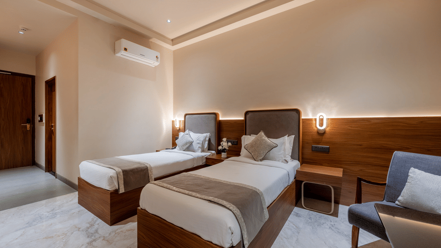 Twin beds with white linens and decorative runners in a modern room at Hotel Highway Prince, Behror, including a work desk and wall-mounted TV.