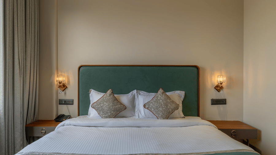 Bedroom at Hotel Highway Prince, Behror, with a teal upholstered headboard, white bedding, accent pillows, and warm bedside wall sconces.