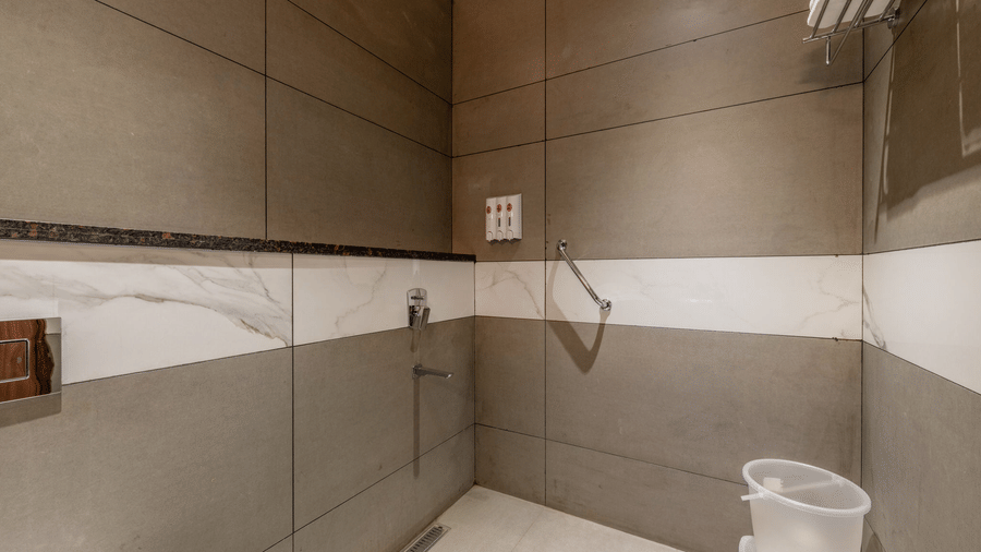 Deluxe Room's bathroom at Hotel Highway Prince, Behror, with tiled walls, a bucket, bathroom fittings, and a towel rack.