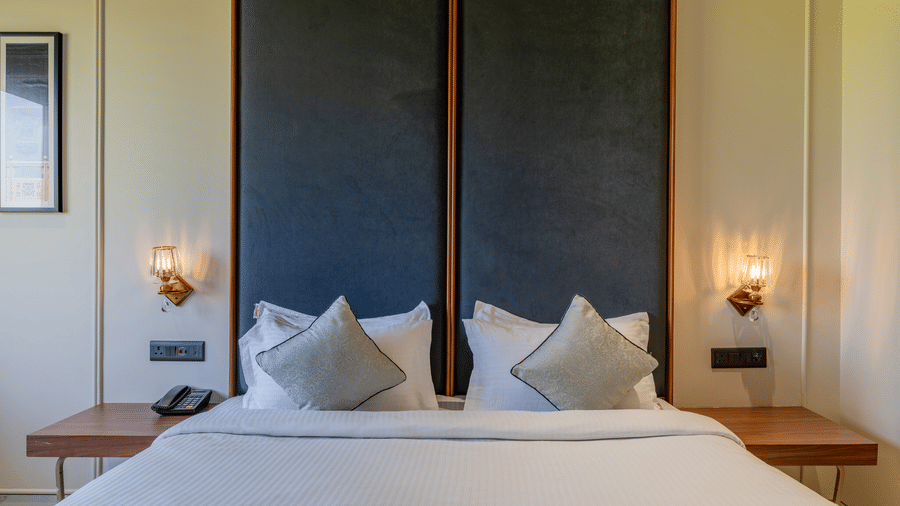 Close-up of a double bed with white linens and gray accents, set against a two-tone blue and cream wall.