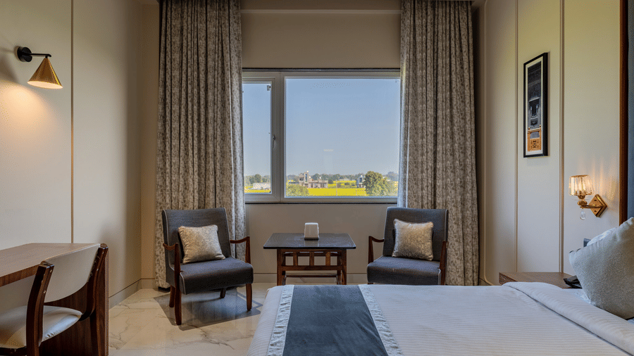 Close-up view at Hotel Highway Prince, Behror of a window flanked by long curtains, two armchairs, and a small wooden coffee table.