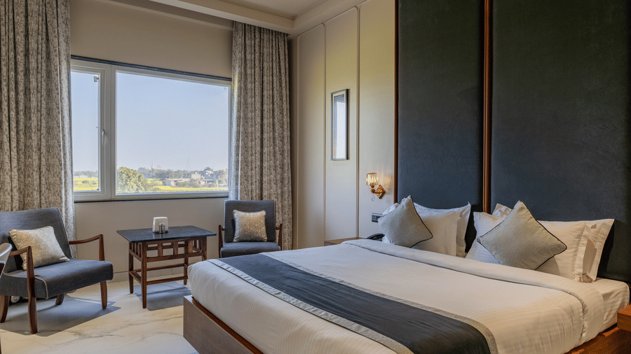 A Hotel Highway Prince, Behror room showing a double bed with a dark headboard, two grey armchairs, and large windows with heavy curtains.