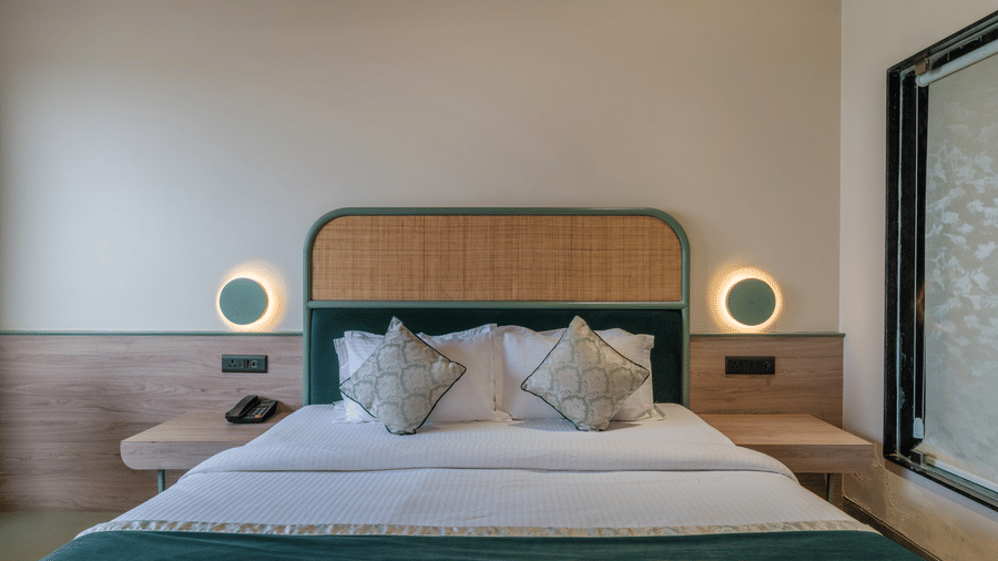 Modern bedroom at Hotel Highway Prince, Behror, showing a king bed with a green headboard, bedside tables with lamps, and wood-paneled walls.