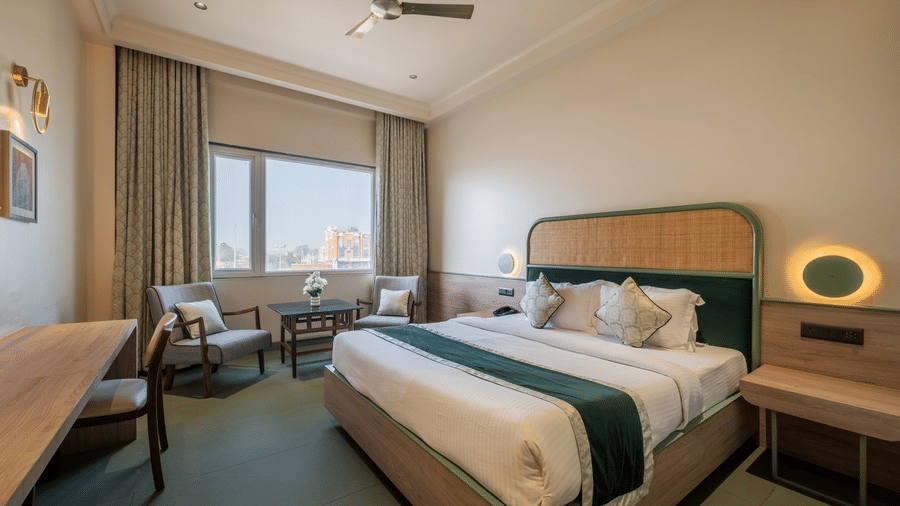 One of the hotel rooms in Behror at Hotel Highway Prince, showcasing a double bed with green runner, a long wooden desk, a ceiling fan, and window seating.