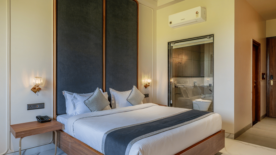  Interior of a Hotel Highway Prince, Behror room with a double bed against a dark paneled wall, flanked by bedside tables and lamps.