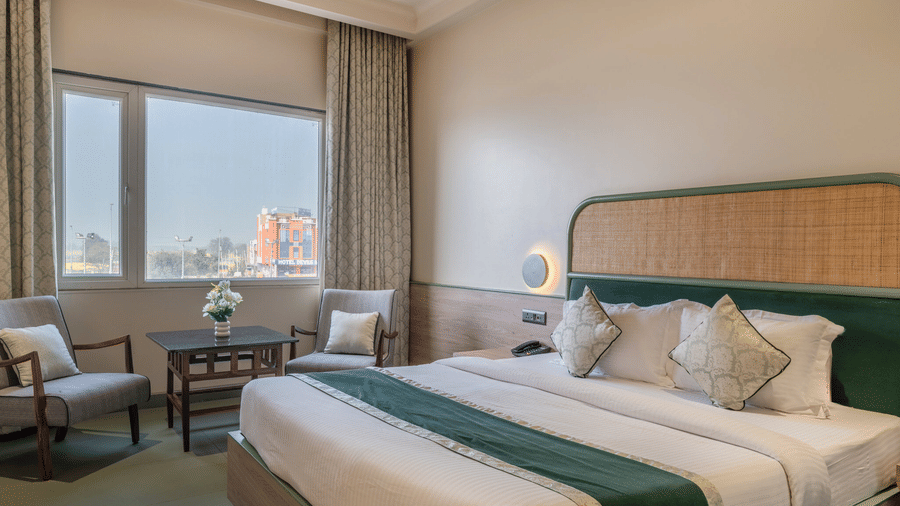 Bright room at Hotel Highway Prince, Behror featuring a double bed with white linens, two grey chairs, and a small table near the window.