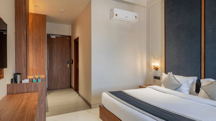 View from the entrance of a Hotel Highway Prince, Behror room showing the bed, a wooden wardrobe, and a hallway leading to the door.