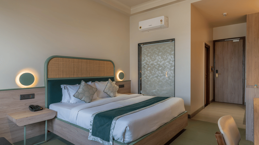 A modern bedroom at Hotel Highway Prince, Behror, featuring a king-size bed with white linens, a teal runner, and a round wall light above the nightstand.