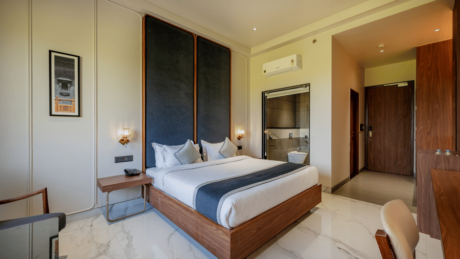 Guest room at Hotel Highway Prince, Behror, with a king bed, dark wall panels, a corner chair, and a view into an adjacent dressing area.