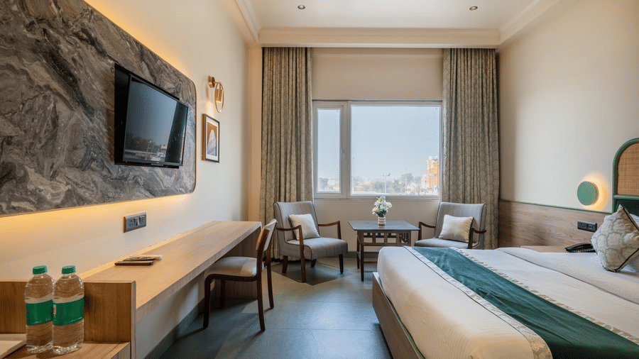 Suite at Hotel Highway Prince, Behror, including a king bed, a long wooden vanity desk with a wall-mounted TV, and a seating area by a window.
