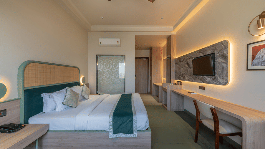 Side view of the Super Deluxe Room at Hotel Highway Prince, Behror, with the double bed facing the all-mounted TV placed on a panel with back lighting.