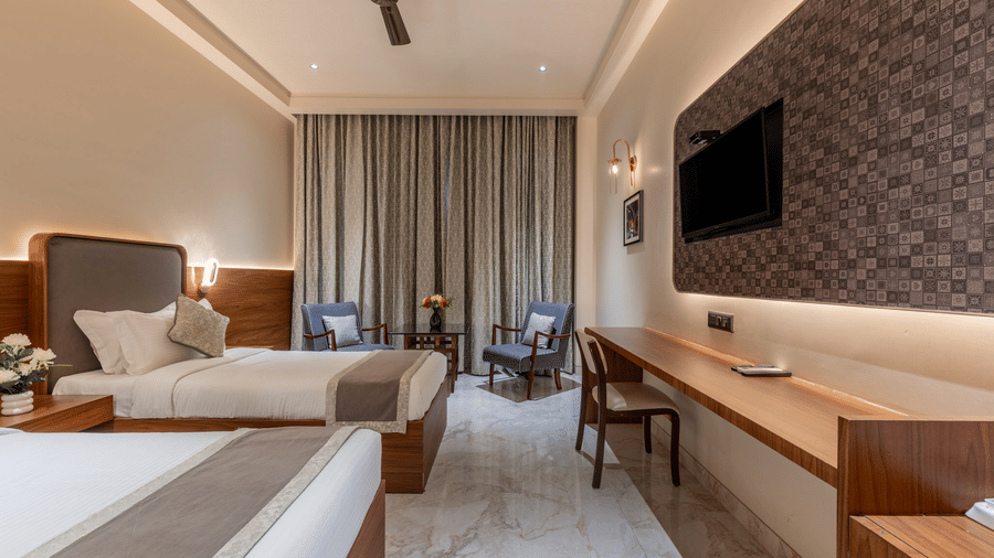 Twin beds in a Superior Room at Hotel Highway Prince, Behror, facing the wall-mounted TV, with a seating area for 2 seen in the back.