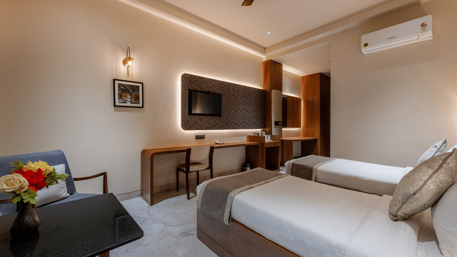 A room view showing two beds, a desk area with a chair, a wall-mounted air conditioner, and framed wall art.