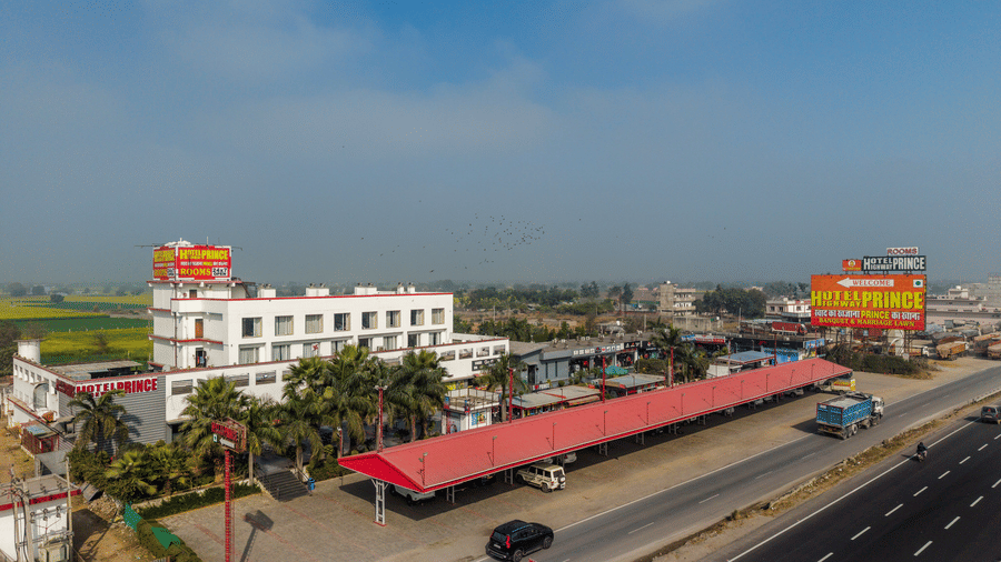 Hotel Highway Prince Paota aerial view showing property along busy highway with red-roofed structures, signage, and surrounding green fields under blue sky.