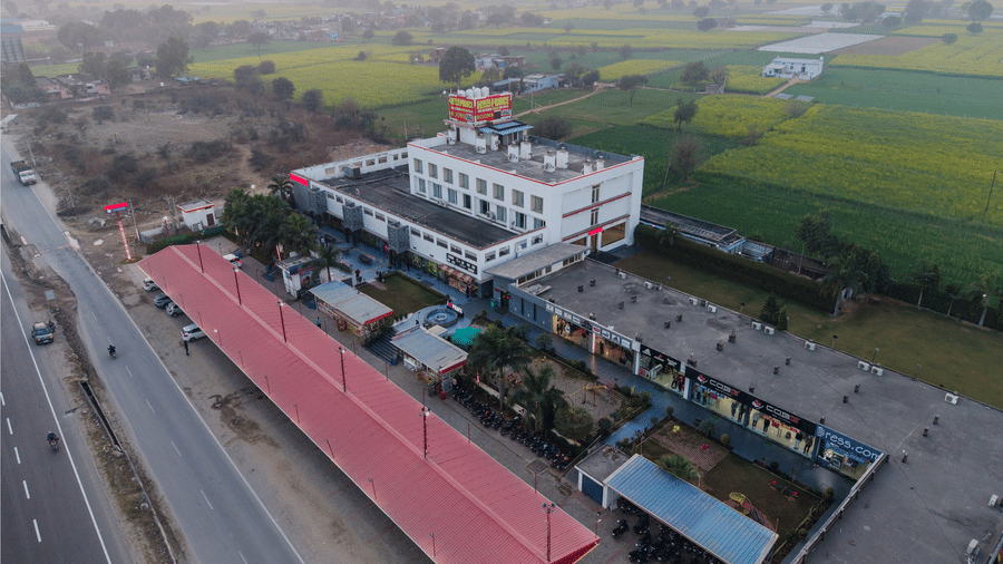 Hotel Highway Prince Paota top aerial view showing full property layout along national highway with red rooftops, green fields, and hazy sky.