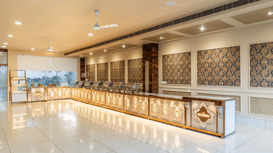 Hotel Highway Prince Paota spacious banquet hall with long decorated buffet counter, patterned wall panels, ceiling fans, and bright recessed lighting.