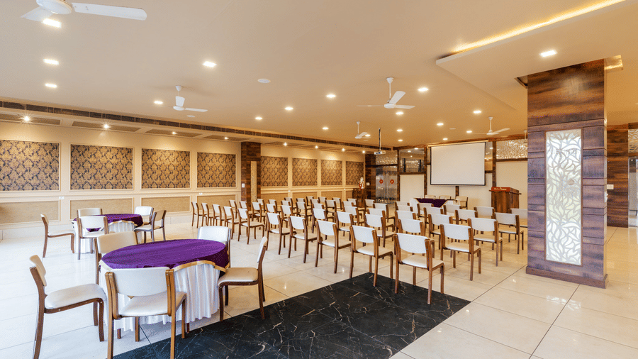 Hotel Highway Prince Paota elegant banquet hall with dark marble flooring, purple-clothed table, white chairs, and bright overhead lighting.