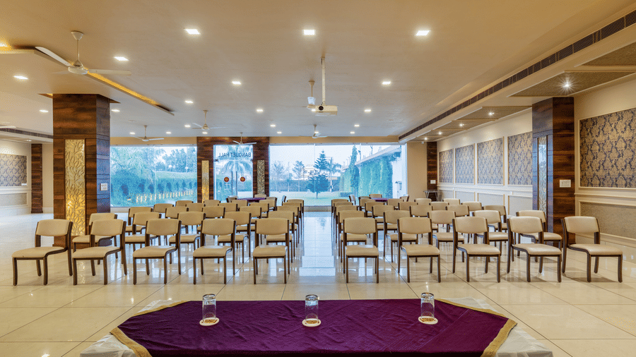 Hotel Highway Prince Paota large banquet hall with purple-draped head table, white chairs in rows, large windows, and warm overhead lighting.