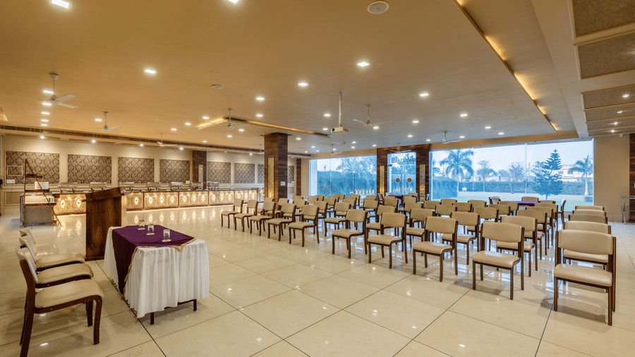 Hotel Highway Prince Paota bright banquet hall with white chairs, purple accent tables, large glass windows, and polished tile flooring.