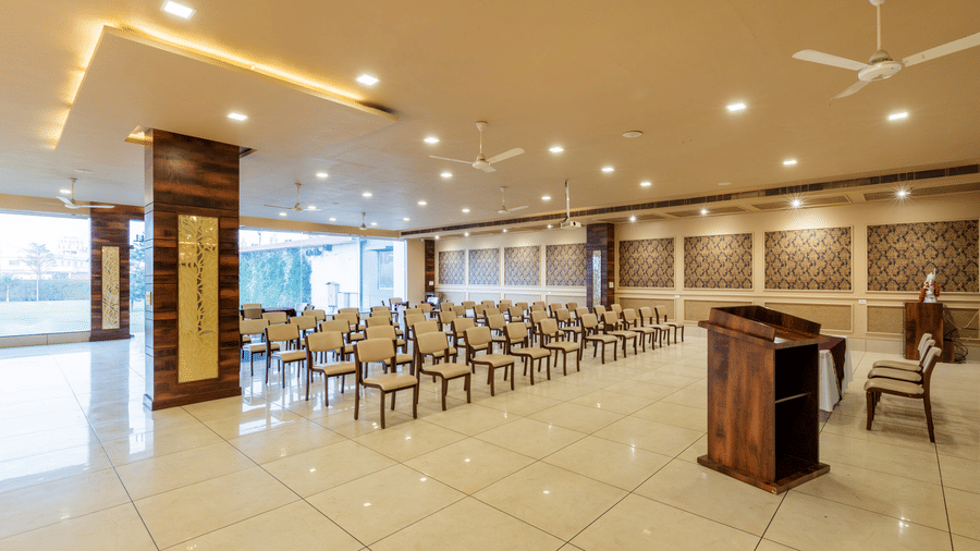 Hotel Highway Prince Paota banquet hall featuring a central wooden podium, rows of white chairs, ceiling fan, and large panoramic windows.