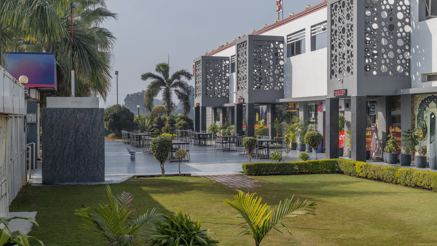 Hotel Highway Prince Paota grand entrance with decorative perforated gate wall, lush green lawn, palm trees, and well-lit exterior at dusk.