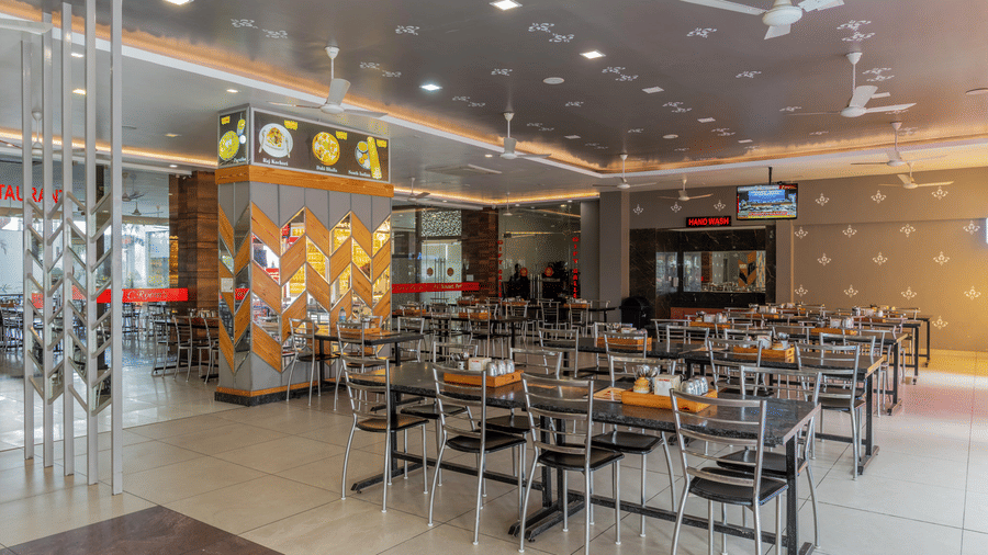 Hotel Highway Prince Paota food court with multiple branded food stalls, dining seating area, decorative ceiling, and vibrant illuminated signboards.