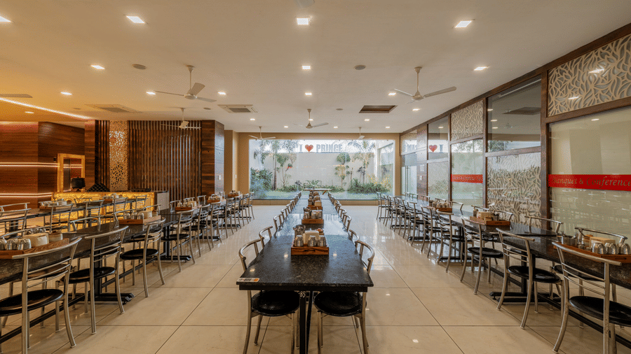 Hotel Highway Prince Paota food court central aisle with long dining tables, black chairs, bright recessed lighting, and food counters on both sides.