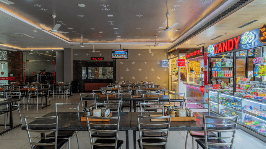 Hotel Highway Prince Paota food court dining area with multiple eatery counters, dark chairs, bright overhead lighting, and vibrant signage displays.