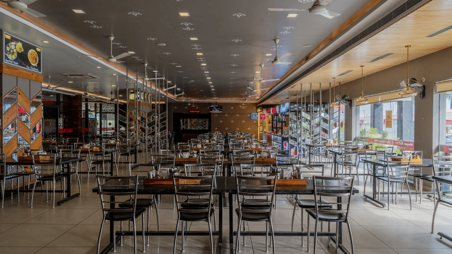 Hotel Highway Prince Paota food court overview with neatly arranged black chairs, dining tables, hanging lights, and multiple eatery counters.