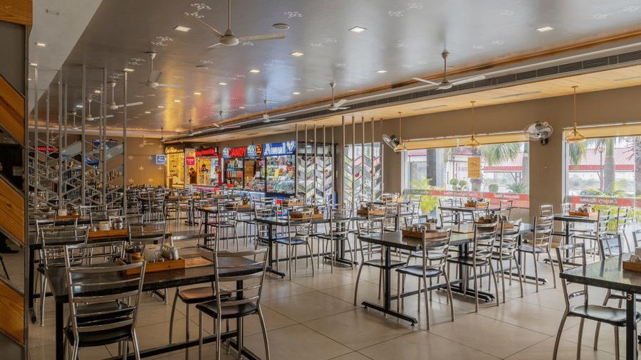 Hotel Highway Prince Paota food court perspective view with rows of black chairs, dining tables, illuminated food stalls, and warm ambient lighting.