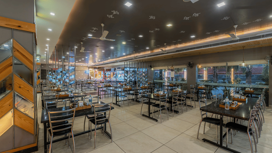 Hotel Highway Prince Paota food court side seating area with wooden wall panels, dark chairs, tiled flooring, and warm overhead lighting.