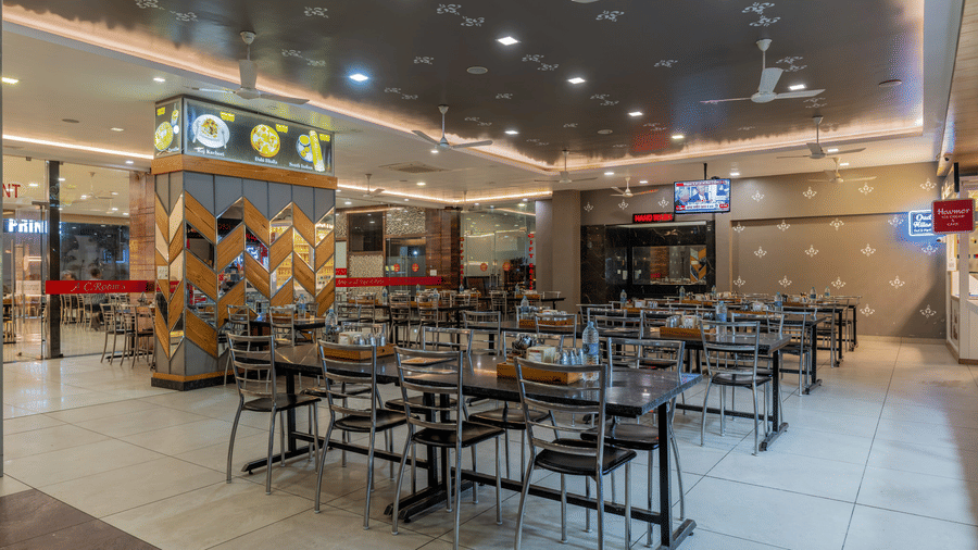 Hotel Highway Prince Paota food court wide-angle view with multiple dining tables, dark chairs, branded food counters, and warm ceiling lighting.