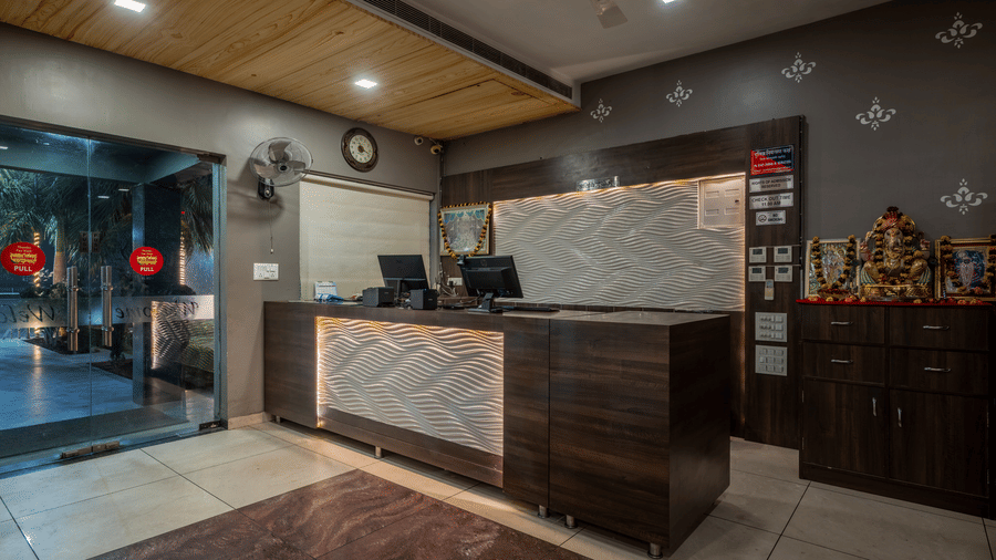 Hotel Highway Prince Paota front desk reception with marble counter, wooden panelling, staff in uniform, wall clock, and warm ceiling lighting.