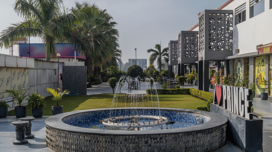 Hotel Highway Prince Paota landscaped entrance garden with circular stone fountain, palm trees, lit hotel signage, and decorative facade.